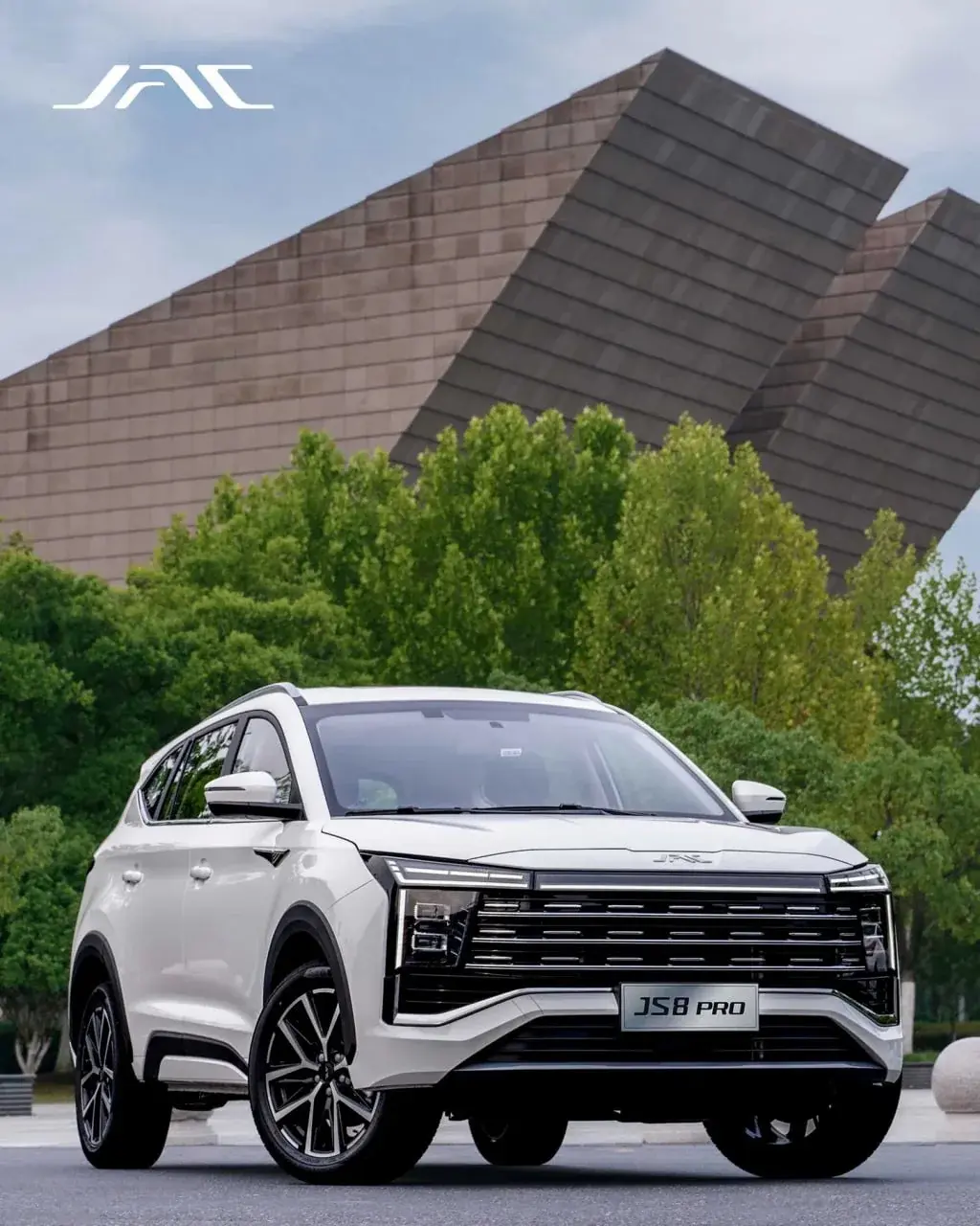 White JAC JS8 Pro in front of angular brick architecture and trees