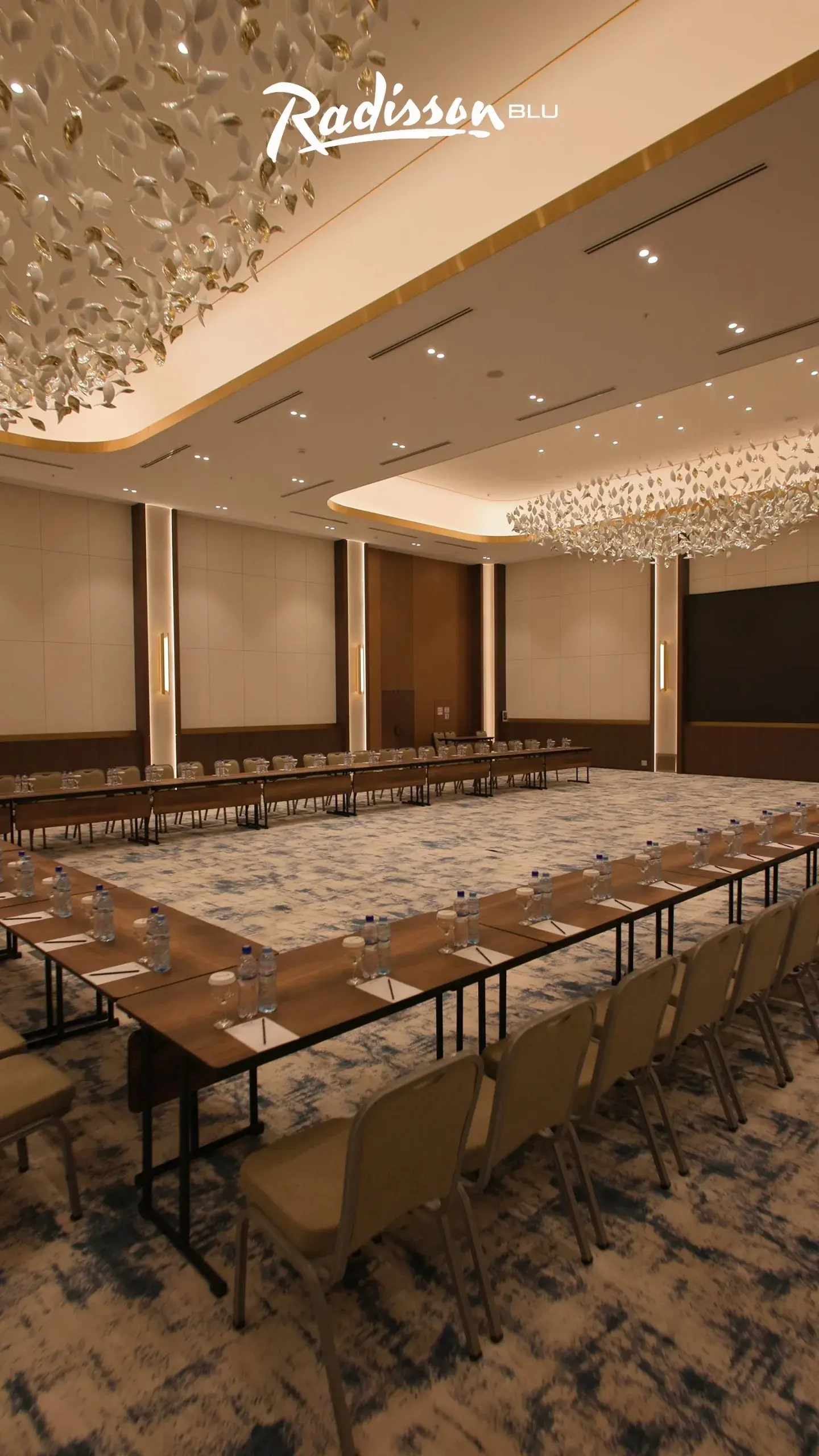 Conference hall with U-shaped tables under leaf-shaped chandeliers